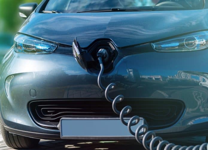 Um carro elétrico moderno conectado a uma estação de carregamento, com o cabo de recarga inserido na lateral do veículo.