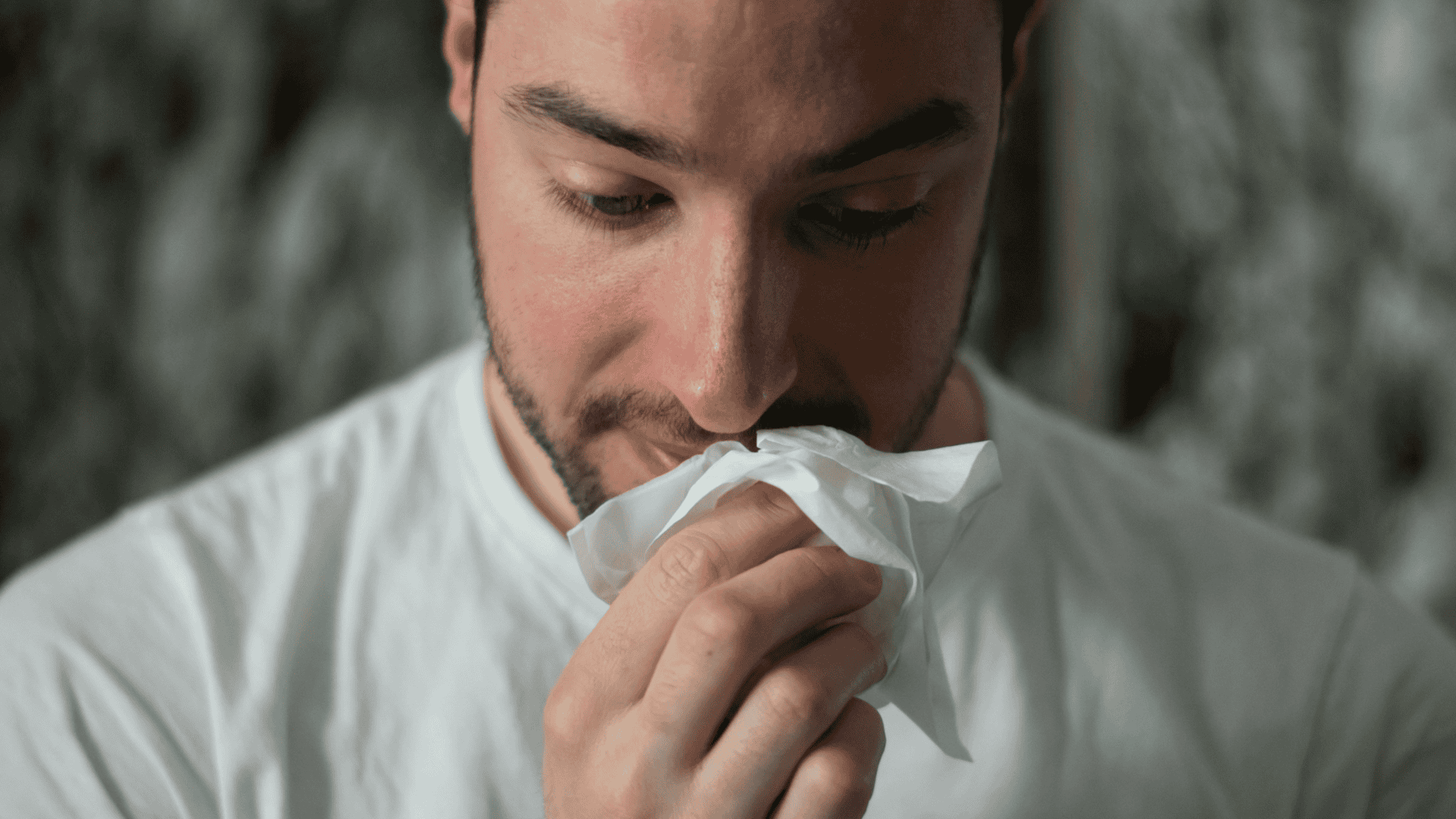imagem mostra um close-up no rosto de um homem, que seguro um lenço embaixo do nariz escorrendo
