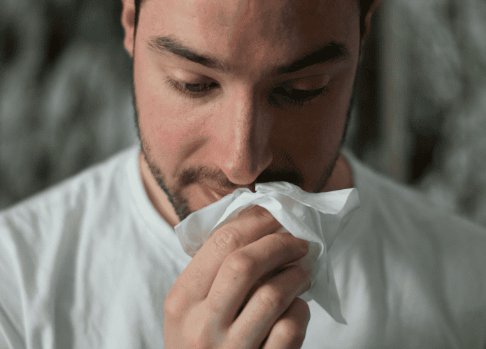 imagem mostra um close-up no rosto de um homem, que seguro um lenço embaixo do nariz escorrendo