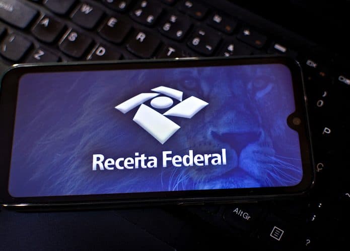 Logo da Receita Federal exibido em um smartphone que está em cima de um teclado de computador