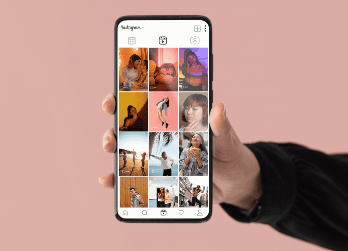 Mão segura um smartphone exibindo o perfil do Instagram, com miniaturas de postagens organizadas em formato vertical