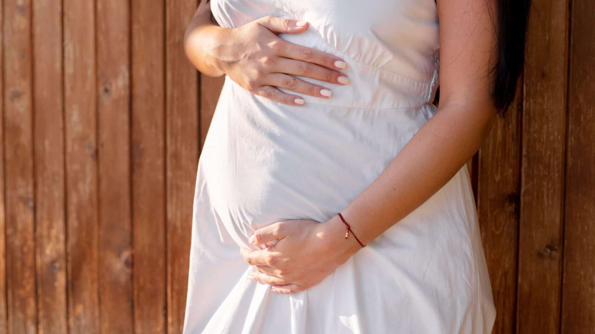 mulher grávida segurando a barriga com vestido branco