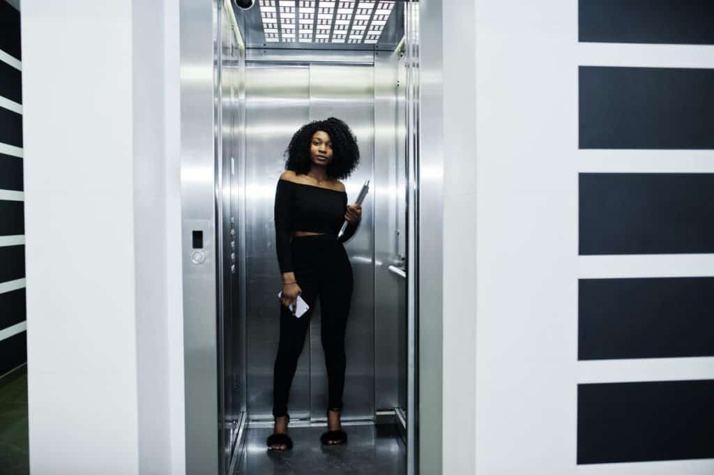mulher sorrindo de preto segurando caderno e celular dentro de elevador