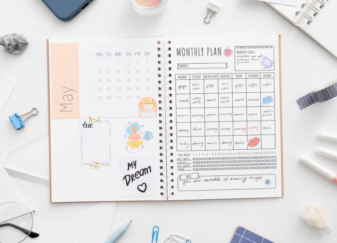 Uma mesa minimalista e funcional com um planner organizado no centro, rodeado por canetas coloridas, óculos de leitura