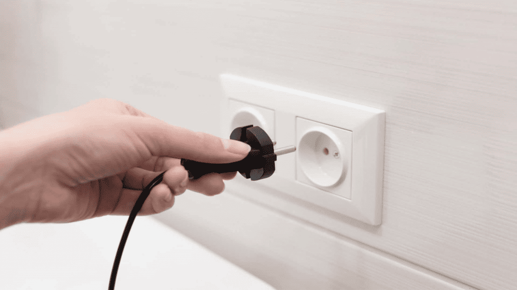 mão de mulher segurando cabo com plugue do dispositivo elétrico para a tomada.