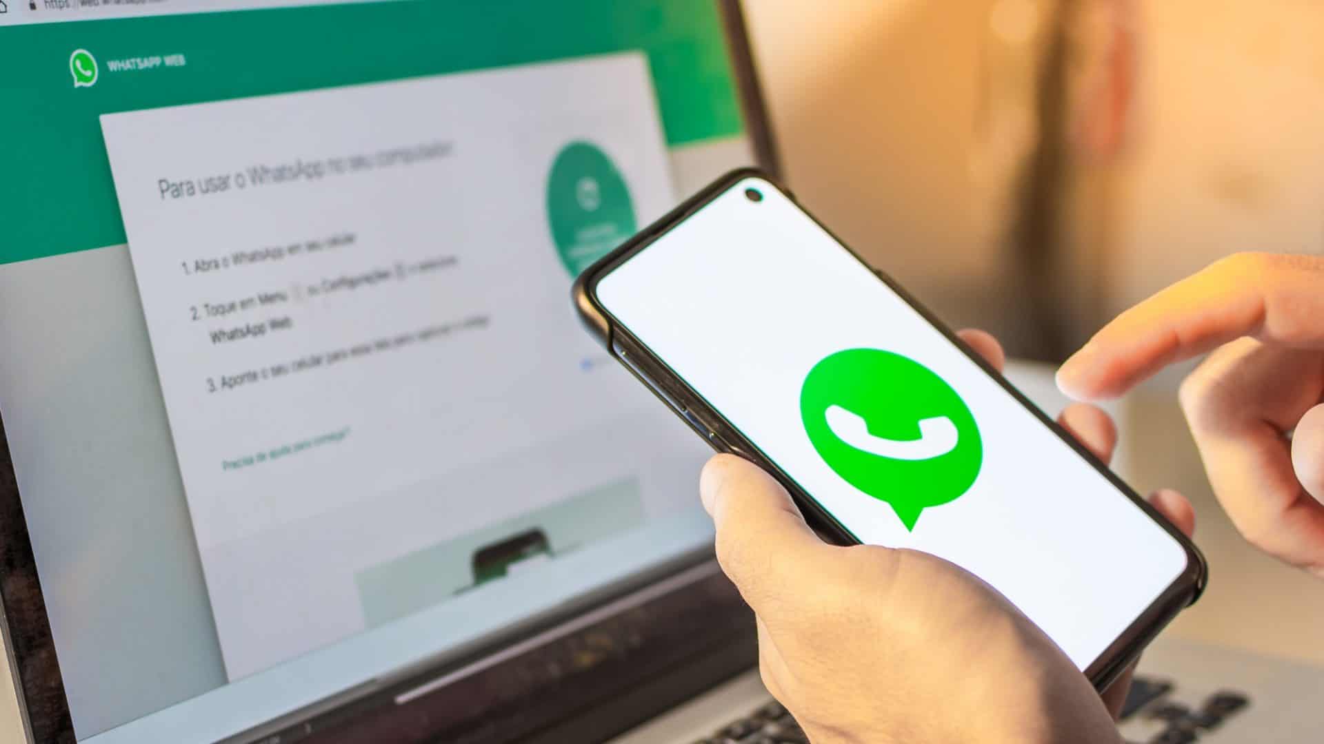 Mãos segurando um dispositivo de telefone celular inteligente com o logotipo do aplicativo da empresa WhatsApp na tela e um notebook com o aplicativo da Web WhatsApp no ​​navegador da Internet