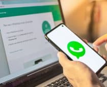 Mãos segurando um dispositivo de telefone celular inteligente com o logotipo do aplicativo da empresa WhatsApp na tela e um notebook com o aplicativo da Web WhatsApp no ​​navegador da Internet