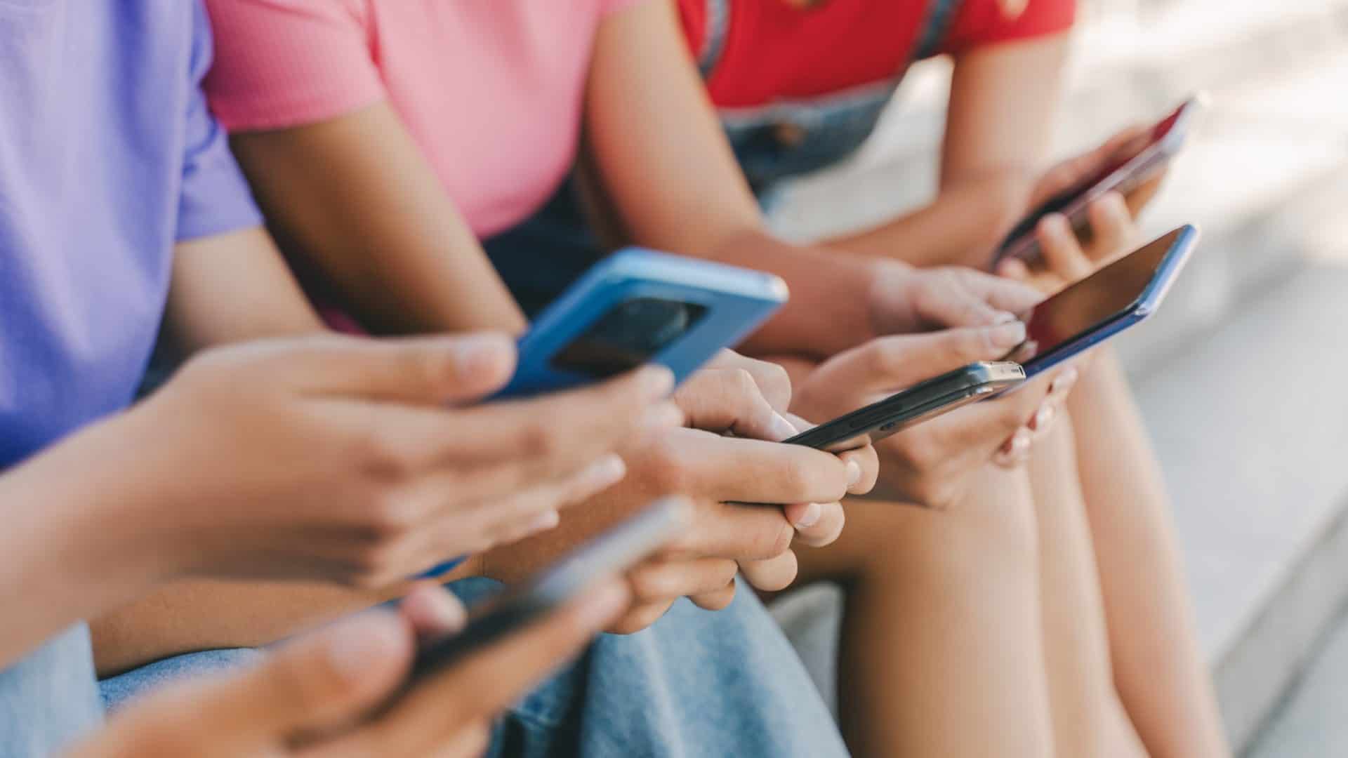 Na imagem, que ilustra matéria sobre Lei que restringe uso de celulares na escola, crianças ou adolescentes seguram seus dispositivos eletrônicos.