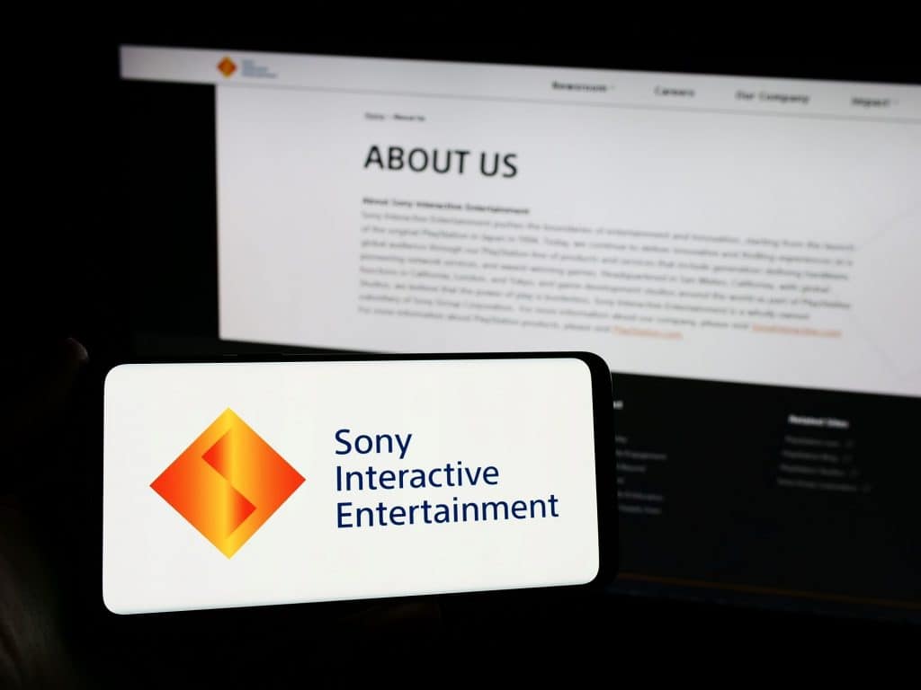 Logo da Sony Interactive Entertainment em um smartphone; atrás, um texto sobre a companhia exibido na tela de um notebook