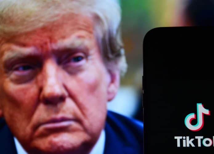 Ao fundo, rosto de onald Trump desfocado; à frente, logo do TikTok em um smartphone