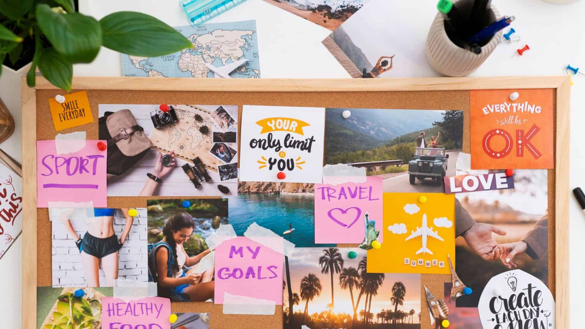 Diversos post-its coloridos, fotos inspiradoras, uma régua e uma planta estão organizados sobre uma mesa branca, compondo um Vision Board