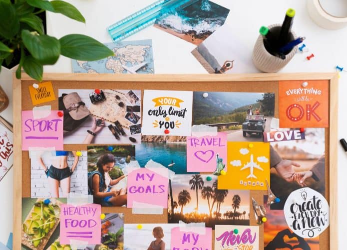Diversos post-its coloridos, fotos inspiradoras, uma régua e uma planta estão organizados sobre uma mesa branca, compondo um Vision Board