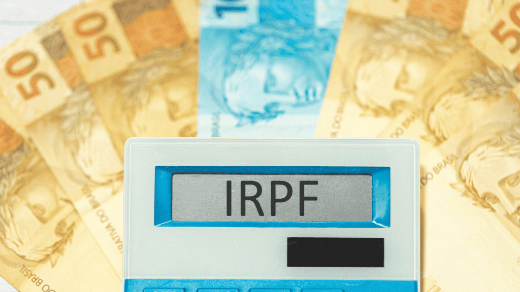 A sigla IRPF refere-se ao Imposto de Renda de Pessoa Física no Brasil, escrita em português brasileiro no visor de uma calculadora com notas de reais na composição. Economia e investimento brasileiros