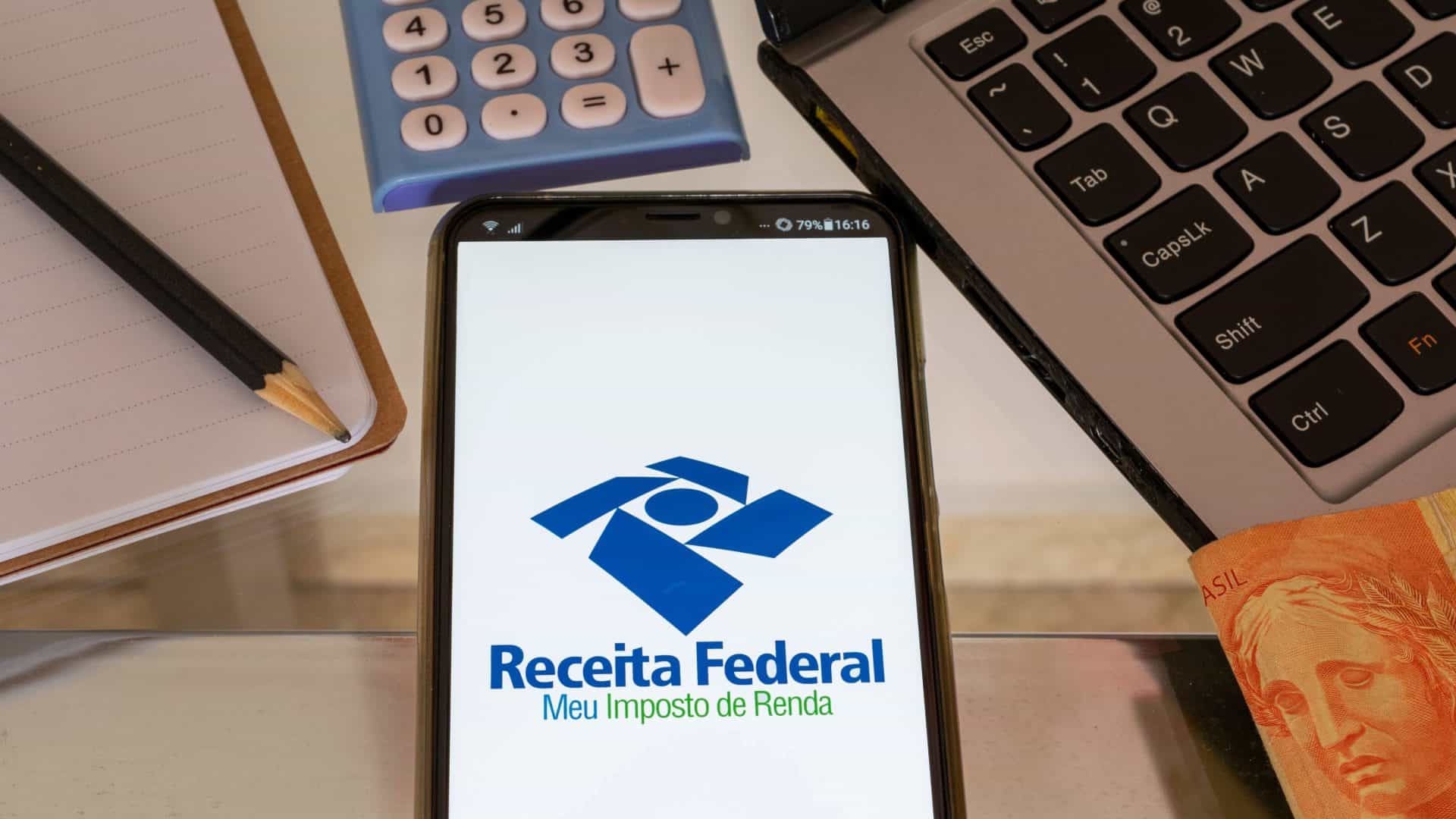 Celular com imposto de renda, Receita Federal, caderno, lápis, calculadora, caderno e moeda brasileira. Declaração de imposto de renda