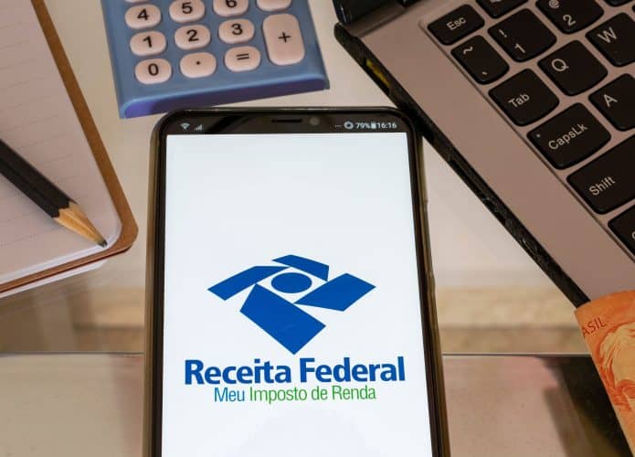 Celular com imposto de renda, Receita Federal, caderno, lápis, calculadora, caderno e moeda brasileira. Declaração de imposto de renda