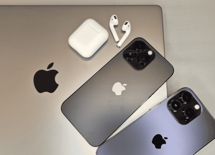 Um MacBook com um par de AirPods e dois iPhones em cima dele