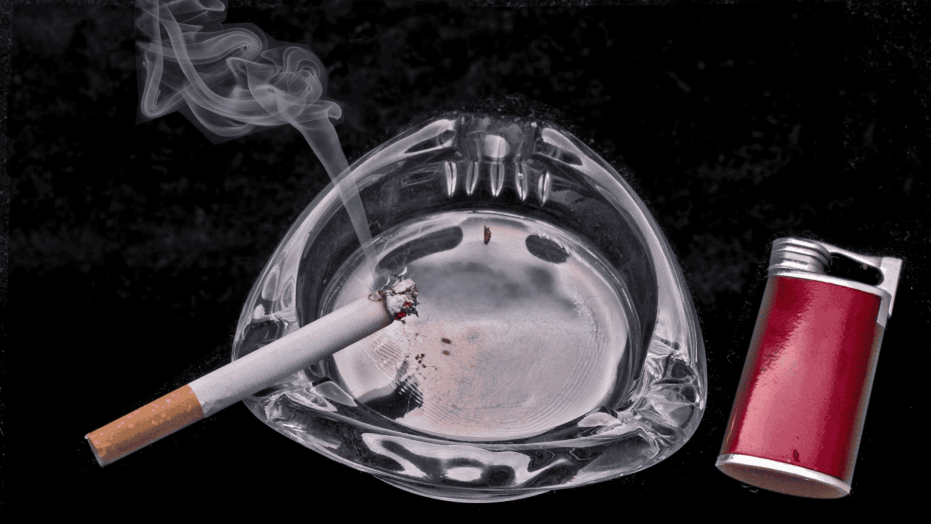 Cigarro apoiado em cinzeiro de vidro, ao lado de isqueiro.