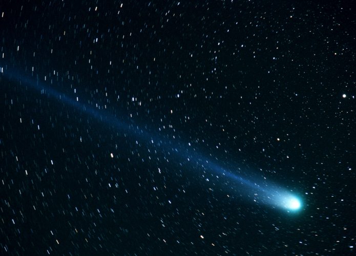 Fotografia do cometa Hyakutake cruzando o céu noturno, com uma cauda azul brilhante se estendendo para trás. O fundo da imagem está repleto de estrelas, algumas com rastros devido ao tempo de exposição. Crédito: Bill Ingalls, Public domain, via Wikimedia Commons.
