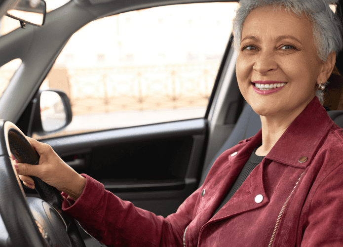 Uma idosa de cabelos cinzas segurando o volante do carro e sorrindo