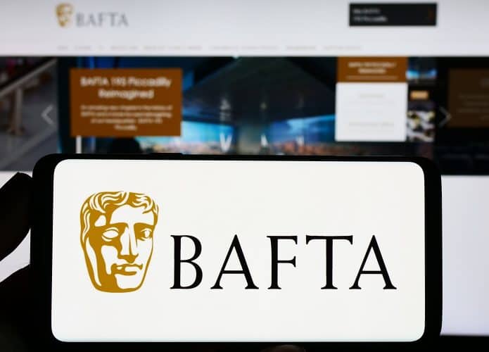 Pessoa segurando celular na horizontal com logotipo do Bafta na tela na frente de monitor exibindo página inicial do site do Bafta