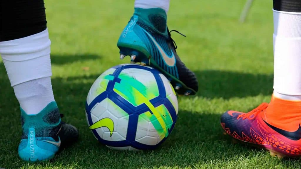 Jogador de futebol com pé em cima de bola enquanto outro jogador está ao seu lado