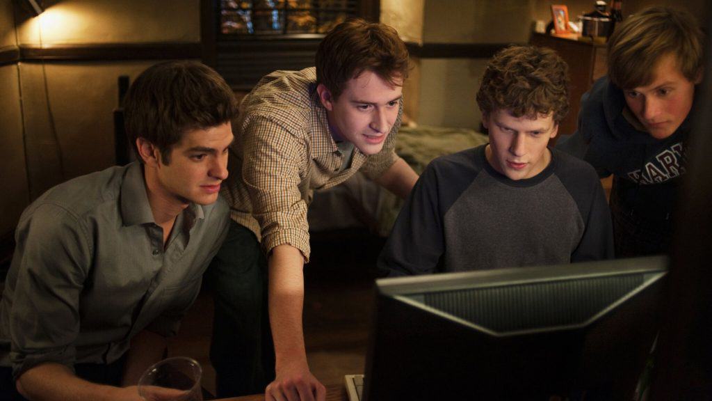 Cena do filme A Rede Social no qual personagens estão em volta de Mark Zuckerberg, interpretado por Jesse Einsenberg, enquanto ele mexe num computador