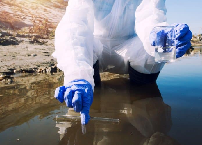 cientista com equipamento de proteção coletando amostra de água