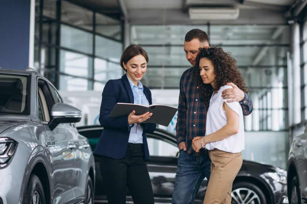 casal com uma vendedora de carros vendo o catálogo