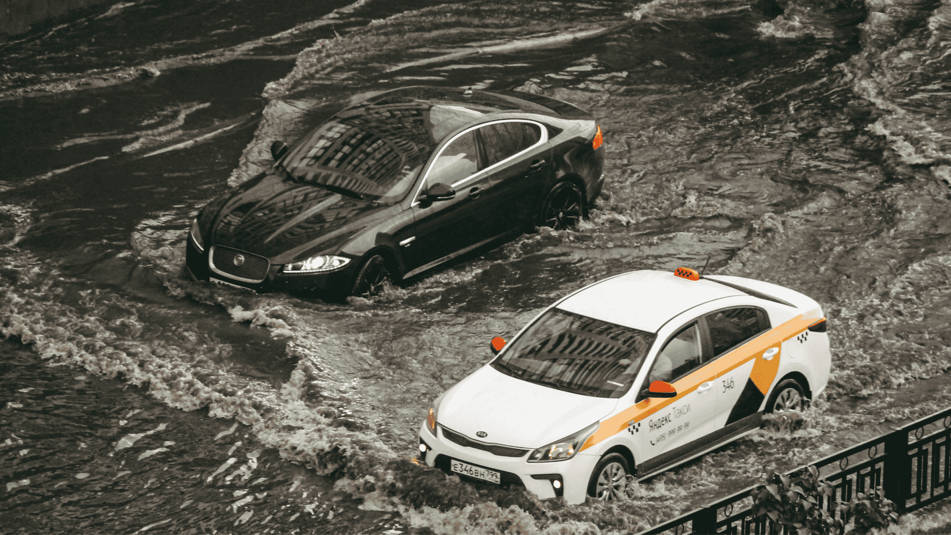 imagem mostra dois carros passando por uma enchente