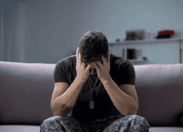 imagem mostra um homem sentado no sofá com as mãos apoiadas no rosto, triste