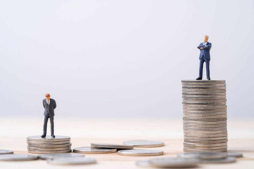 Dois montes de moedas, sendo que, o da direita, é maior; em cima de ambos, estão duas figuras masculinas