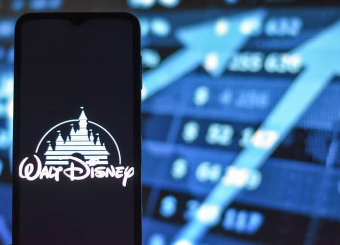 Logo da Walt Disney em um smartphone; ao fundo, gráficos com ações