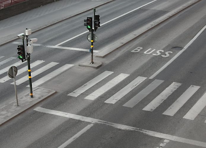 Imagem ilustrativa de cruzamento em rua com semáforo e faixa de pedestre