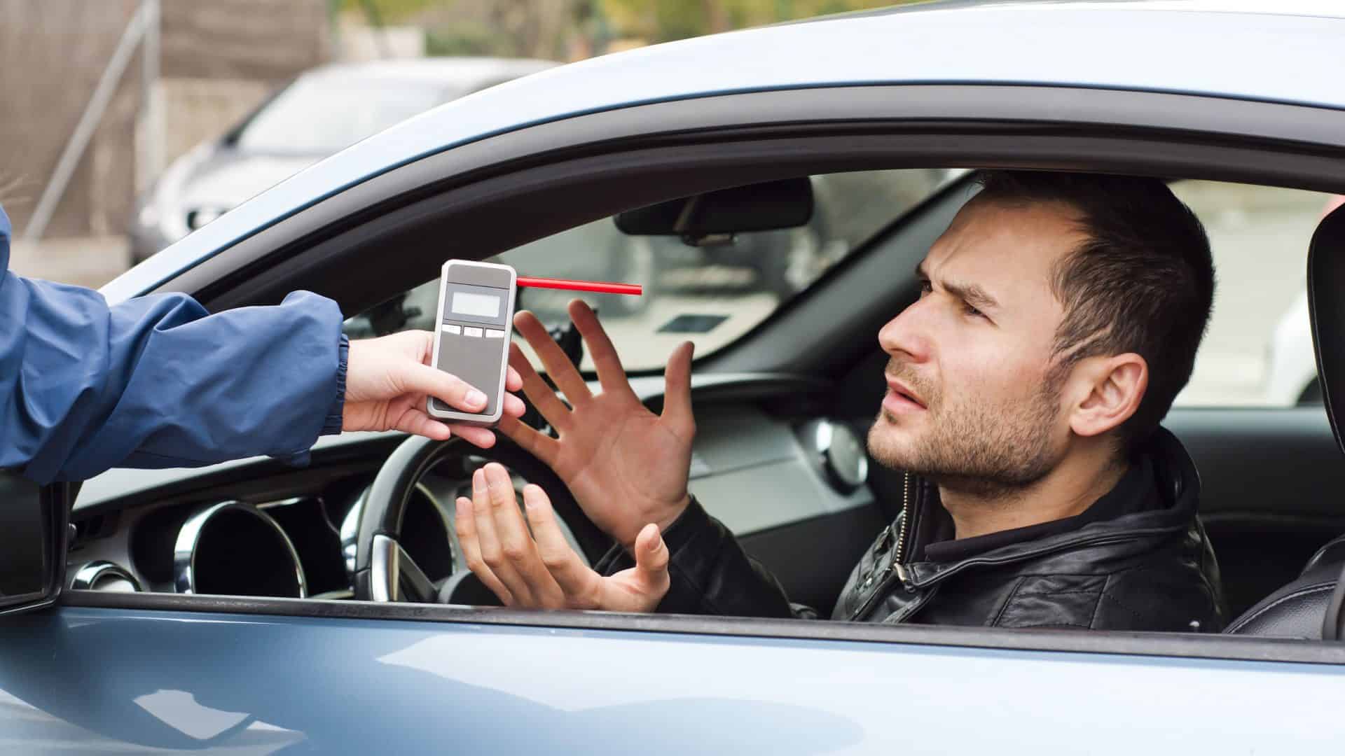 Homem fazendo o teste do bafômetro no carro