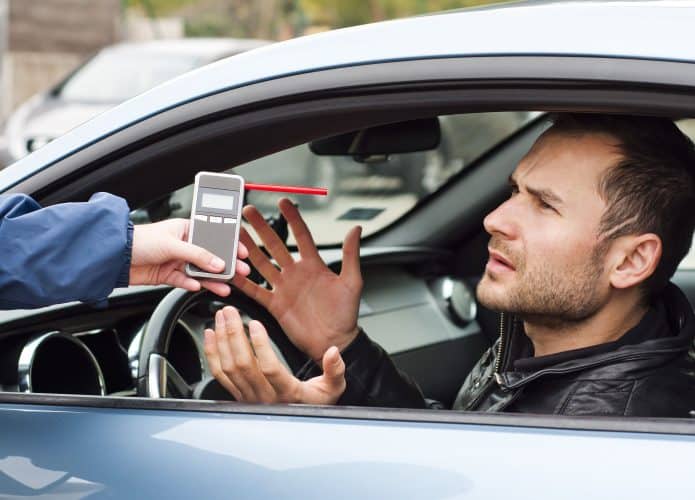 Homem fazendo o teste do bafômetro no carro
