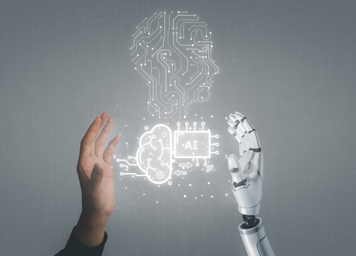 Mãos de humano e de robô espalmadas; entre elas, a representação de uma cabeça humana formada por circuitos e um chip de computador escrito 