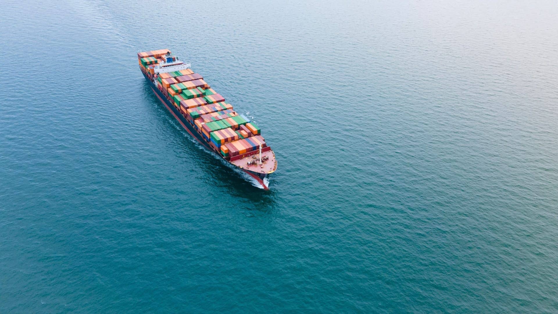 imagem mostra um grande navio cargueiro navegando sobre a água azul de um mar aberto