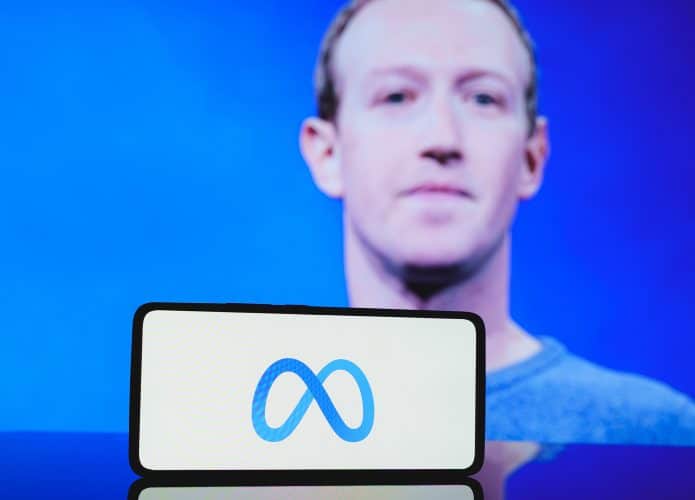 Ao fundo, foto desfocada de Mark Zuckerberg; à frente, logo da Meta em um smartphone