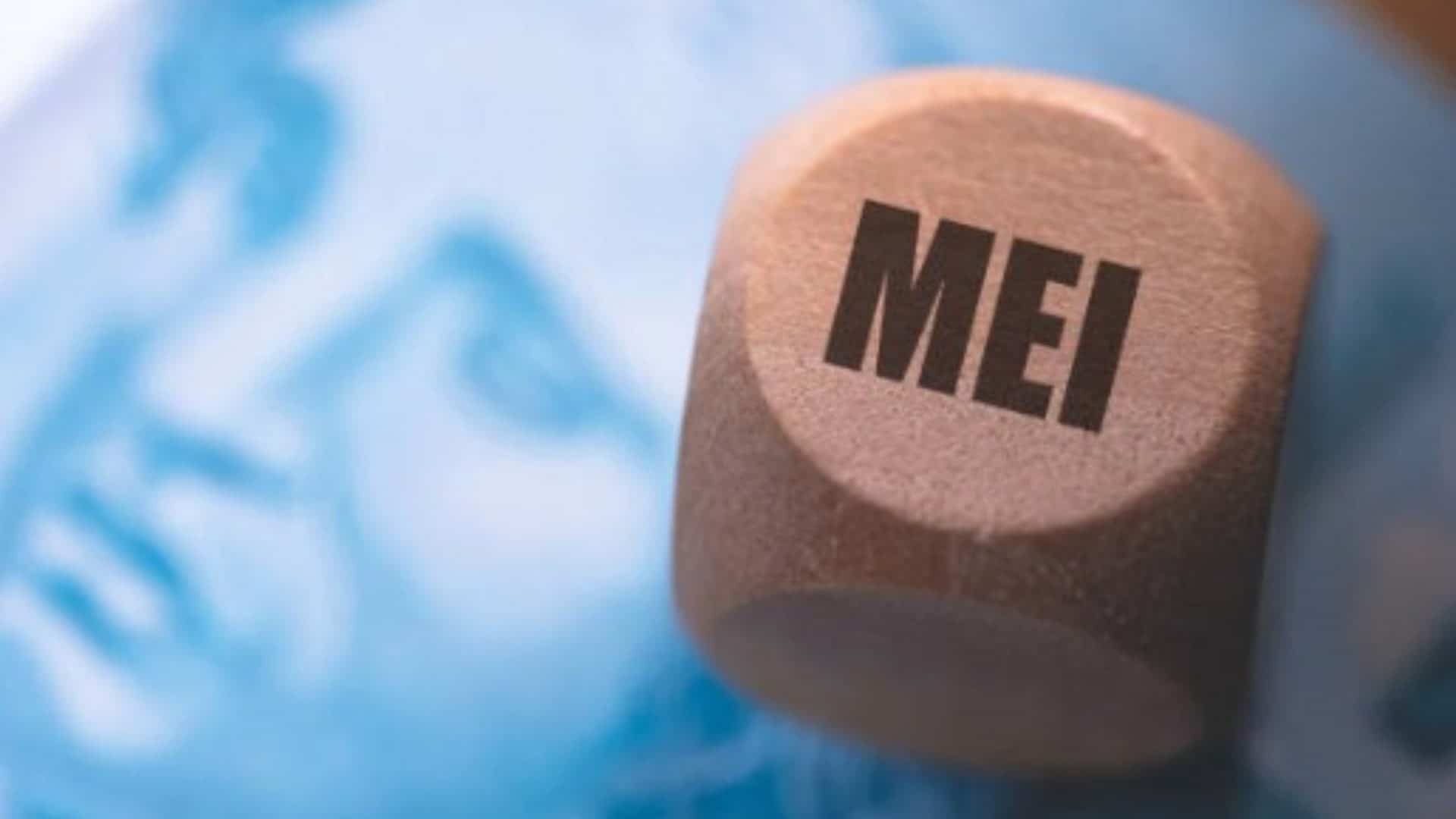 objeto de madeira com a sigla MEI em cima de uma nota de real