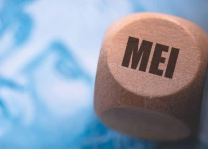 objeto de madeira com a sigla MEI em cima de uma nota de real