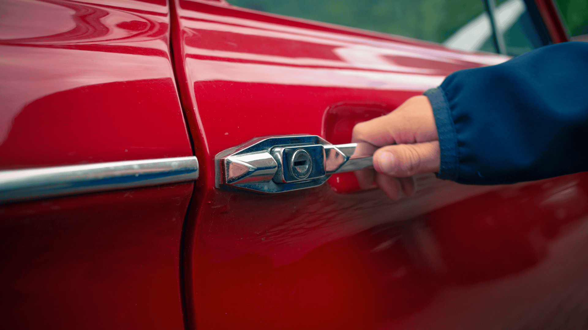 imagem mostra uma pessoa segurando na maçaneta da porta de um carro vermelho