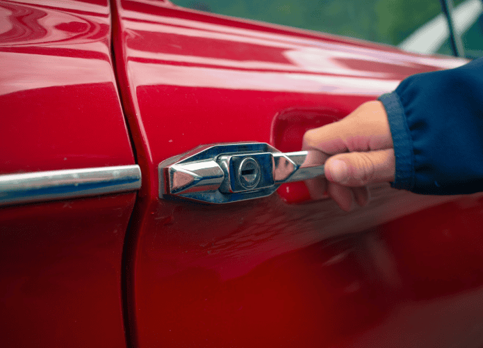 imagem mostra uma pessoa segurando na maçaneta da porta de um carro vermelho