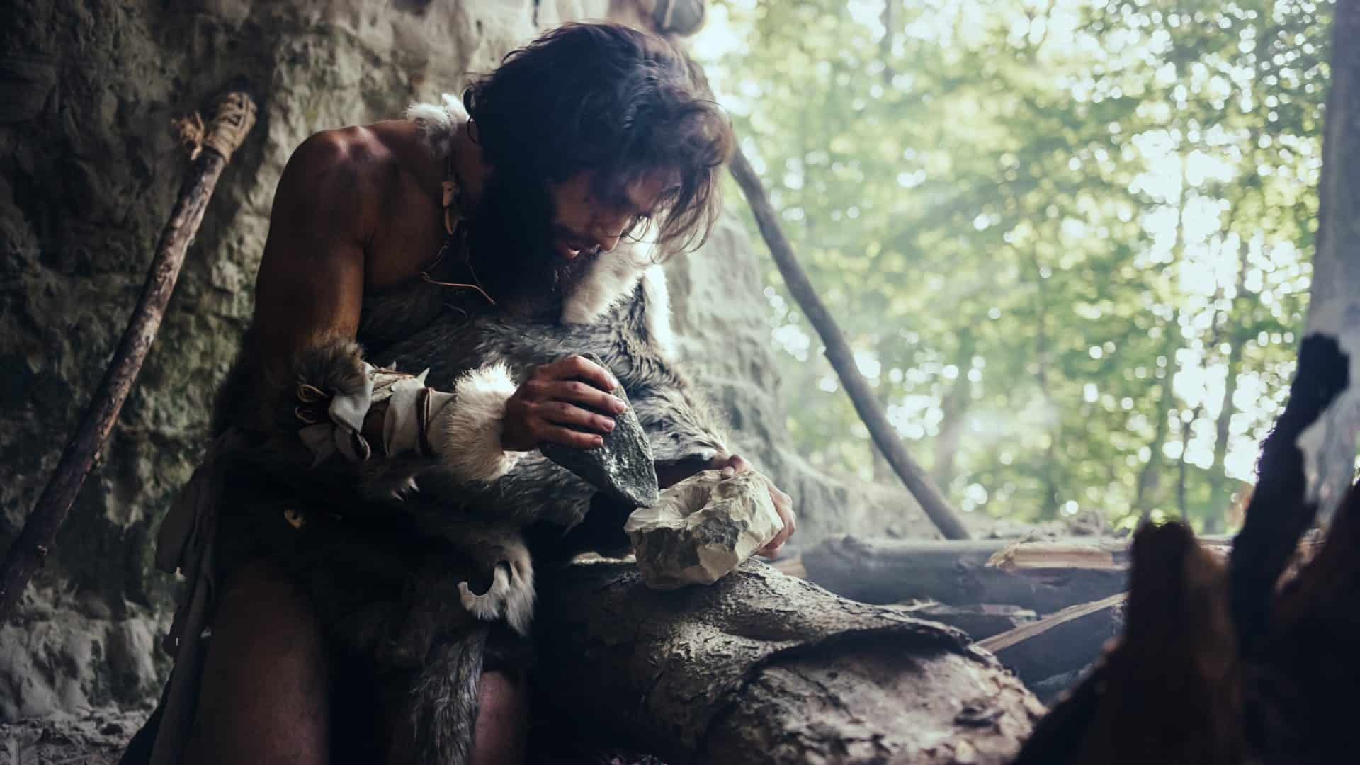 Homem-das-cavernas, dentro de caverna, lascando uma pedra