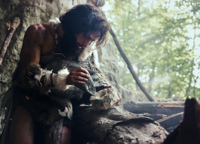Homem-das-cavernas, dentro de caverna, lascando uma pedra