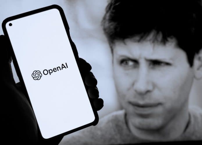 Pessoa segurando celular com logomarca da OpenAI na tela na frente de monitor exibindo foto do CEO da empresa, Sam Altman