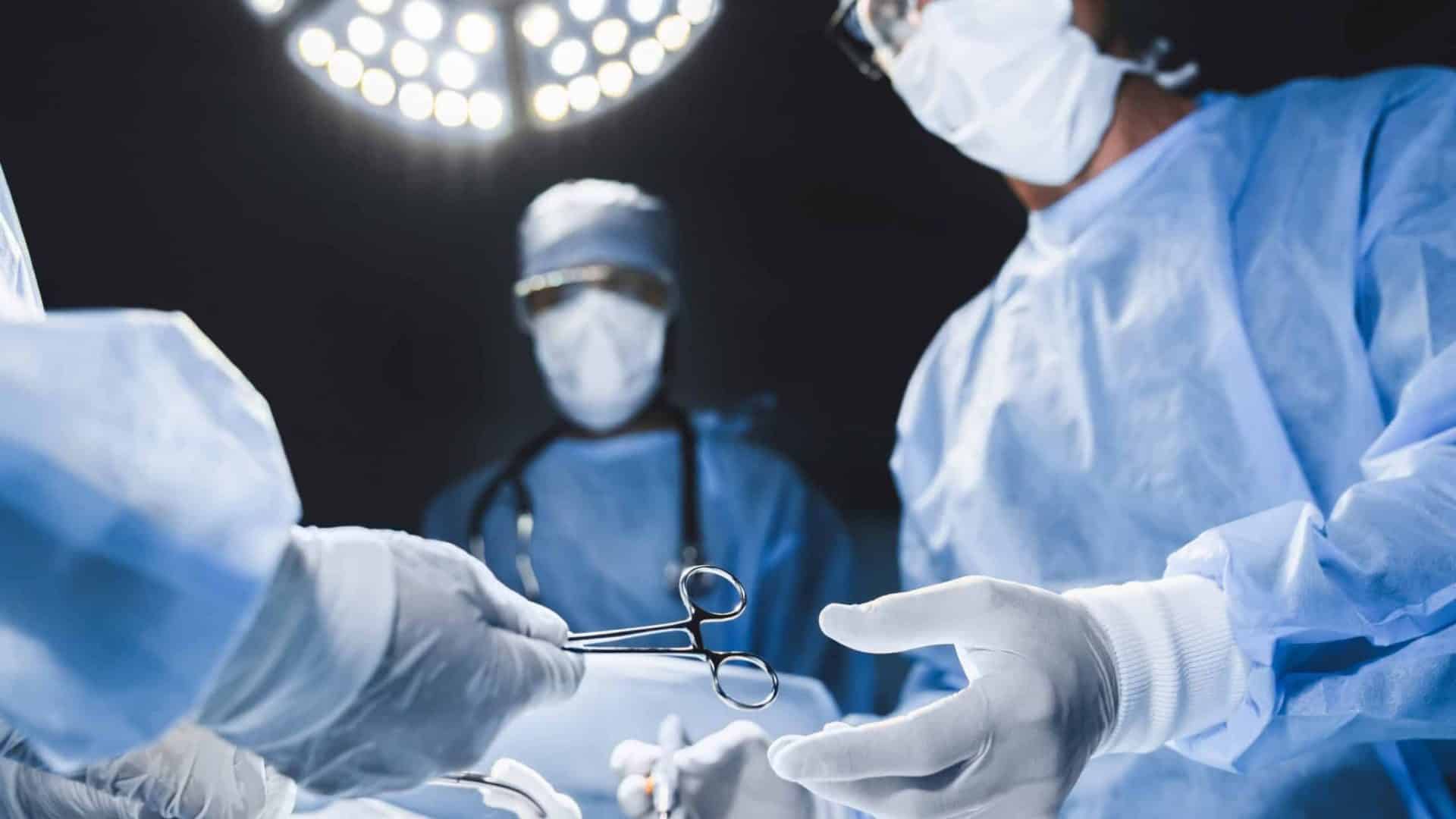 Médicos cirurgiões durante uma cirurgia passando instrumentos com uma luz vinda de cima