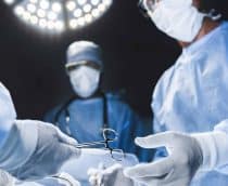 Médicos cirurgiões durante uma cirurgia passando instrumentos com uma luz vinda de cima