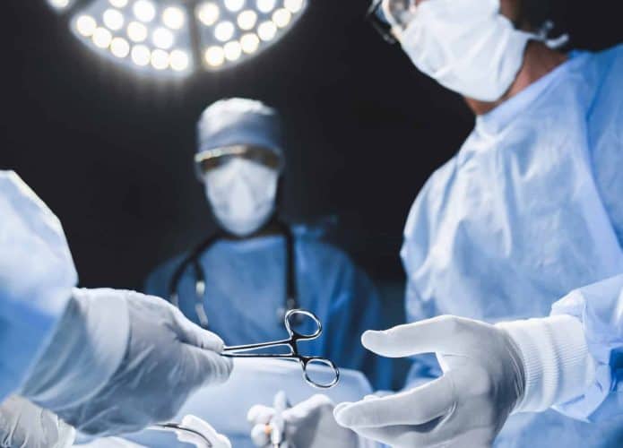 Médicos cirurgiões durante uma cirurgia passando instrumentos com uma luz vinda de cima
