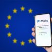 Ao fundo, desfocada, a bandeira da União Europeia; à direita, pessoa segurando um smartphone, no qual é exibida uma página da Meta