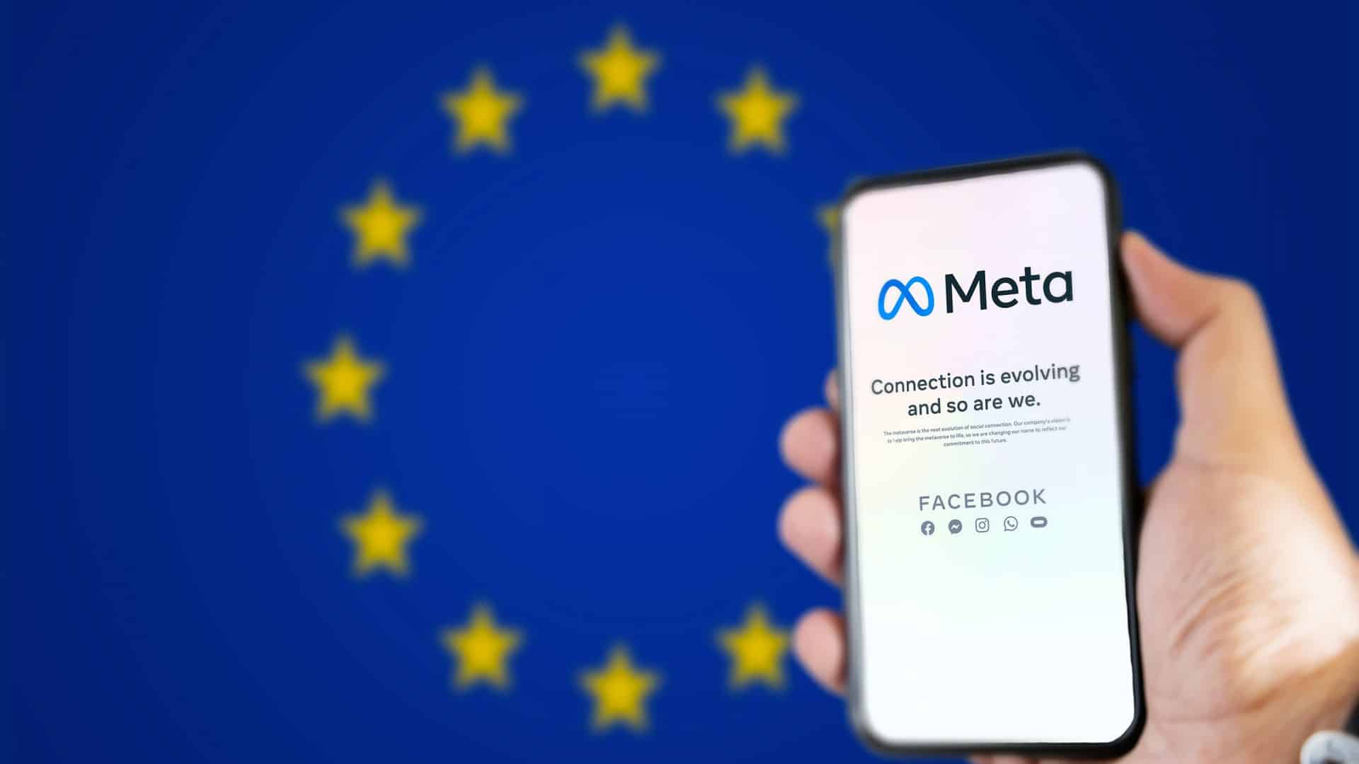 Ao fundo, desfocada, a bandeira da União Europeia; à direita, pessoa segurando um smartphone, no qual é exibida uma página da Meta